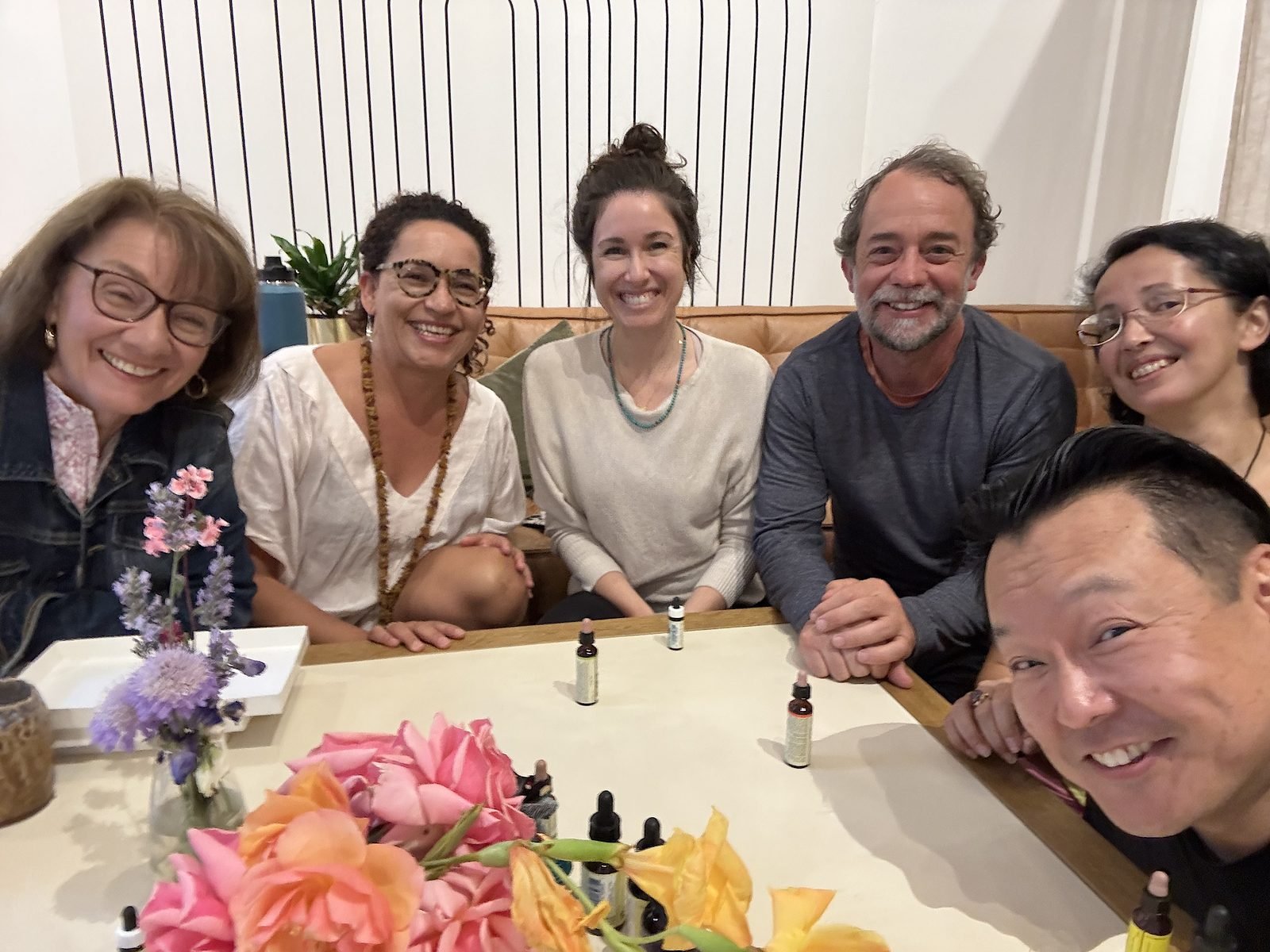 A group gathered around a table with flowers and botanical tinctures